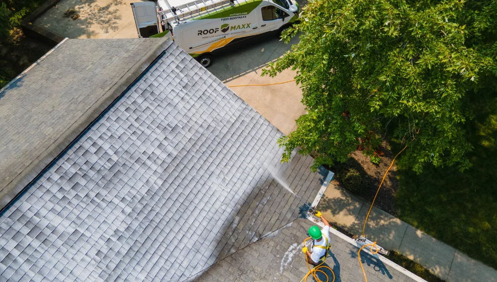 A roofer applies Roof Maxx rejuvenation treatment to an asphalt shingle roof.
