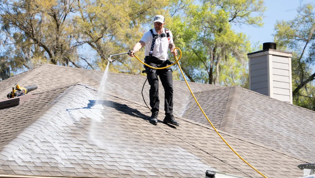 A certified Roof Maxx dealer sprays the all-natural application on a beige asphalt shingle roof on a sunny day in Florida.