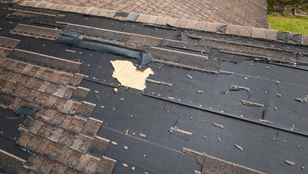 A residential home with severely damaged shingles and large patches of missing shingles.
