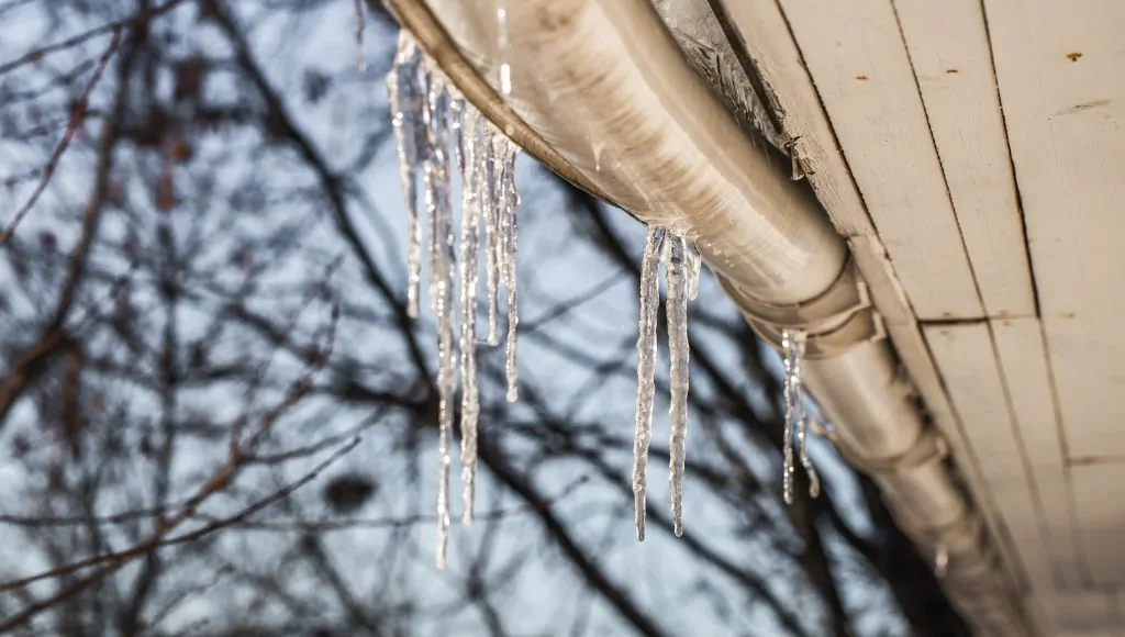 Icicles hang from a sagging metal gutter that is pulling away from the roofline.